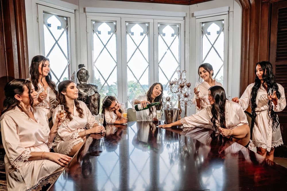 A group in matching pink robes gathers by large windows during wedding day preparations.