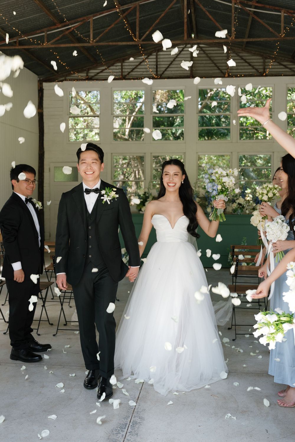 Newlyweds celebrate under a covered pavilion as flower petals rain down during their joyful wedding ceremony.