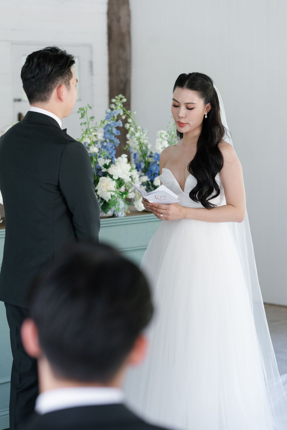 A couple exchanges vows during an elegant wedding ceremony with white floral arrangements.