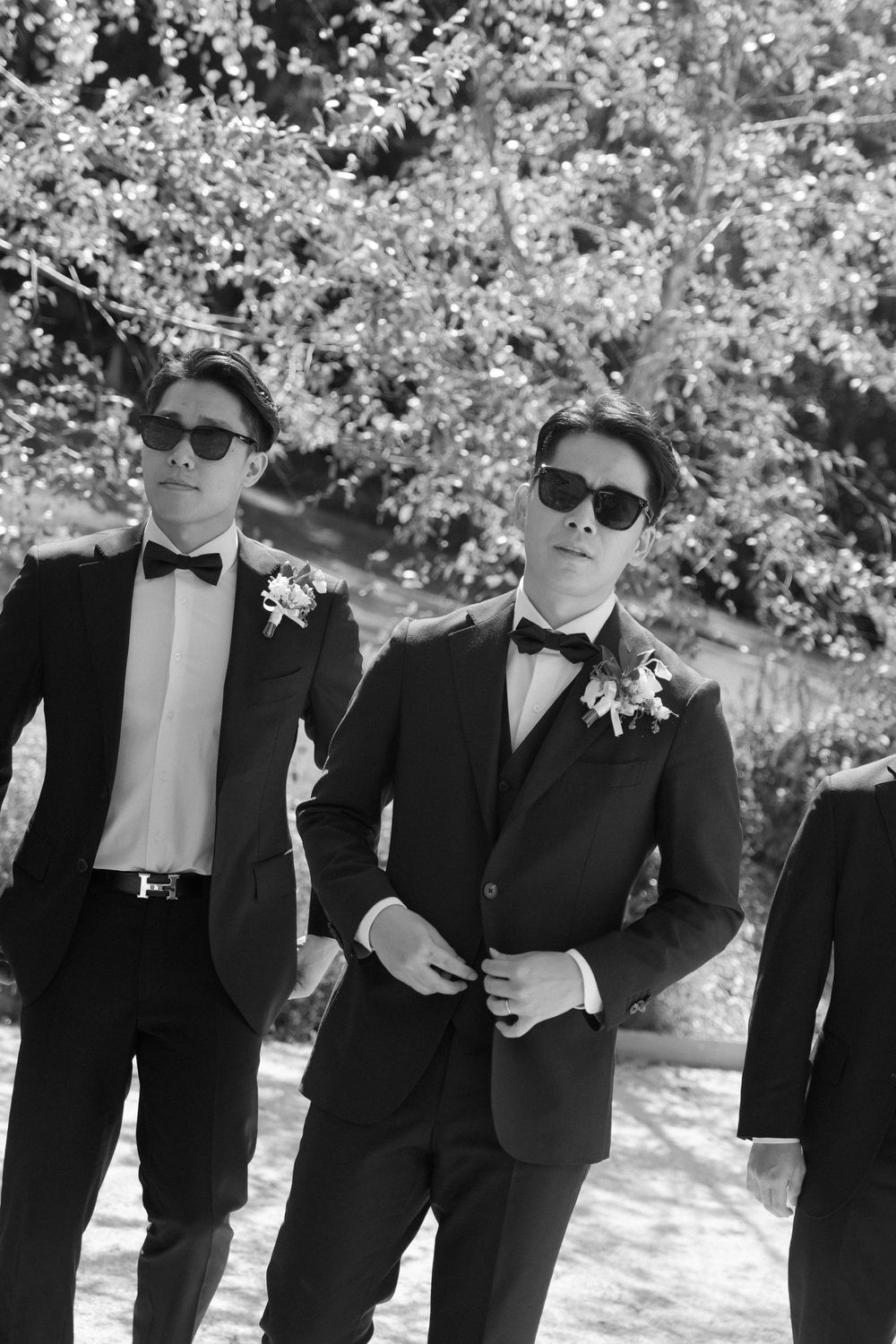 Groomsmen in black tuxedos and sunglasses pose under cherry blossom trees.