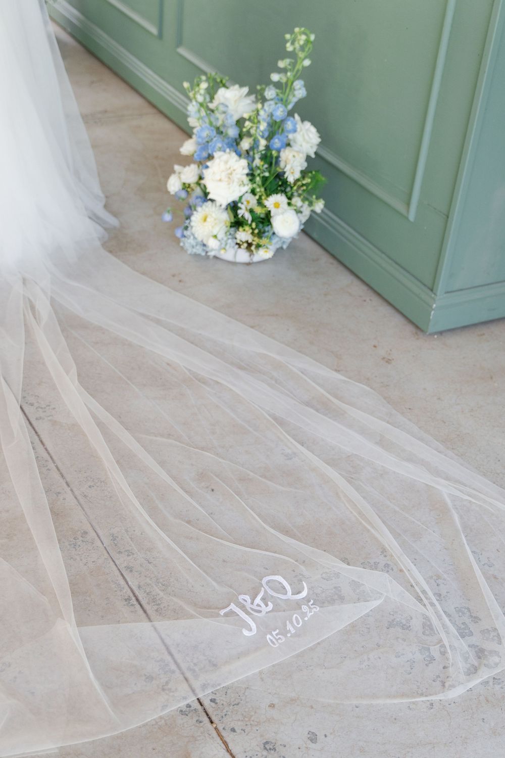 A flowing white bridal veil with delicate lace trim trails elegantly across a light wooden floor.