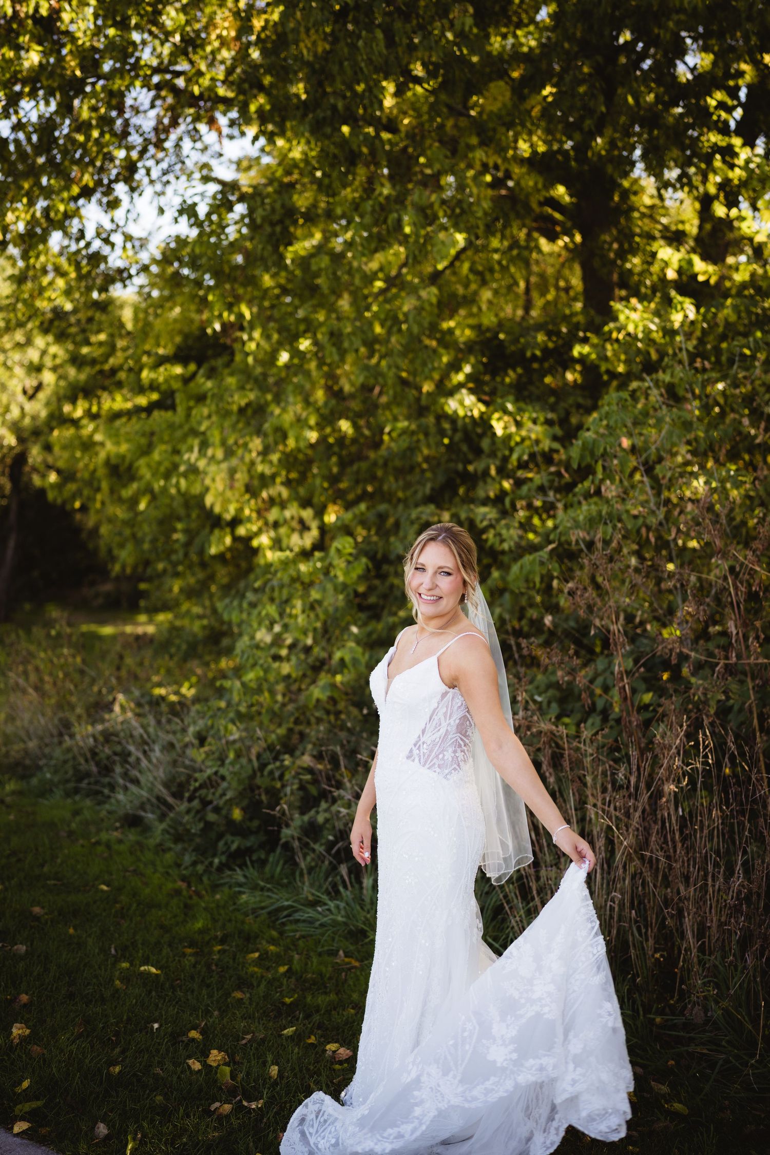 A bride in a flowing white lace dress twirls gracefully in a sunlit garden setting during golden hour.