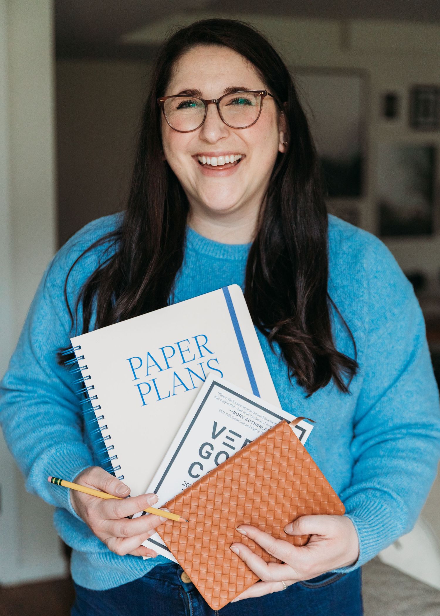 Person in bright blue sweater holding white spiral notebooks against an orange woven background in a progression of poses.