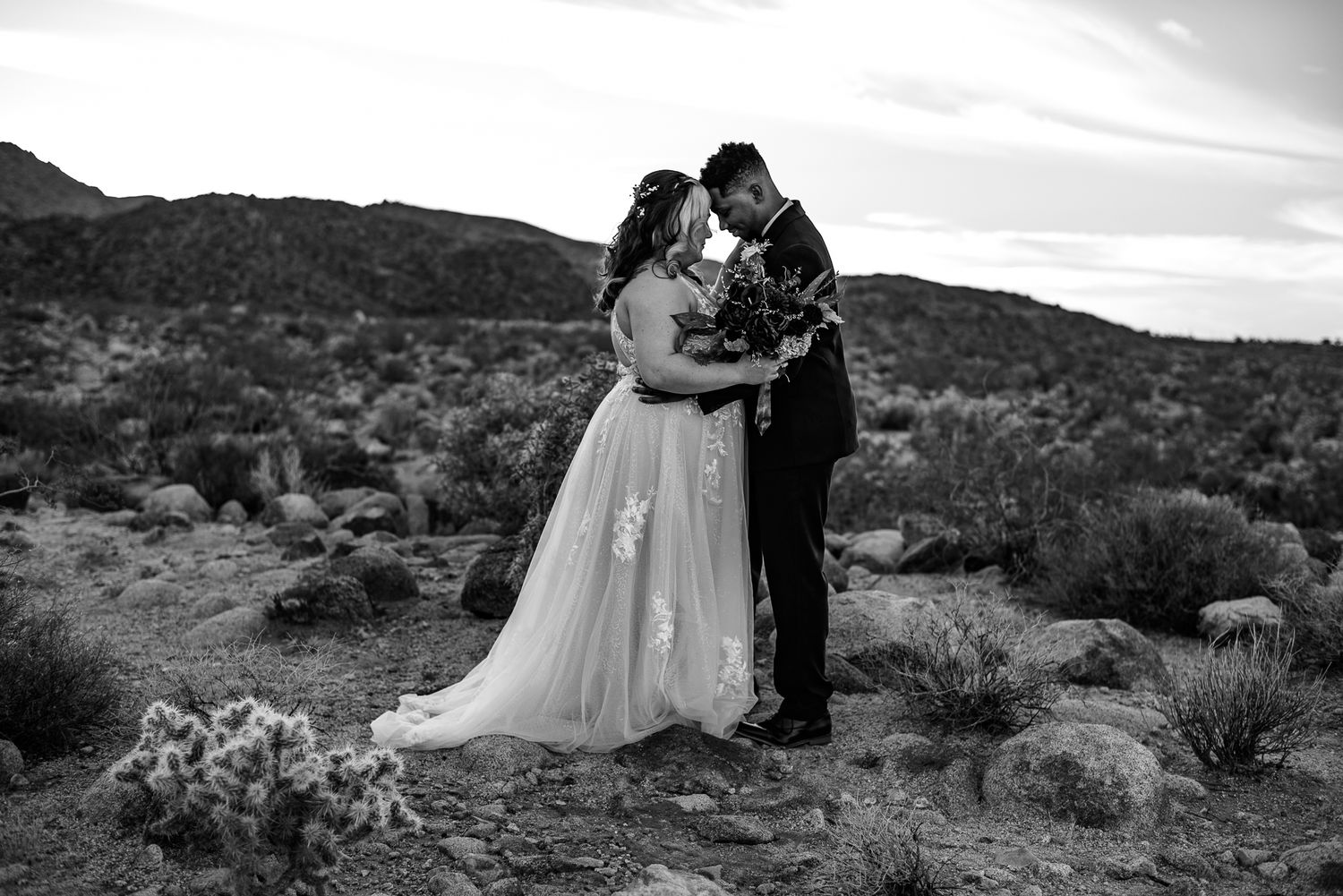 Couple facing each other in the desert with hills behind them.