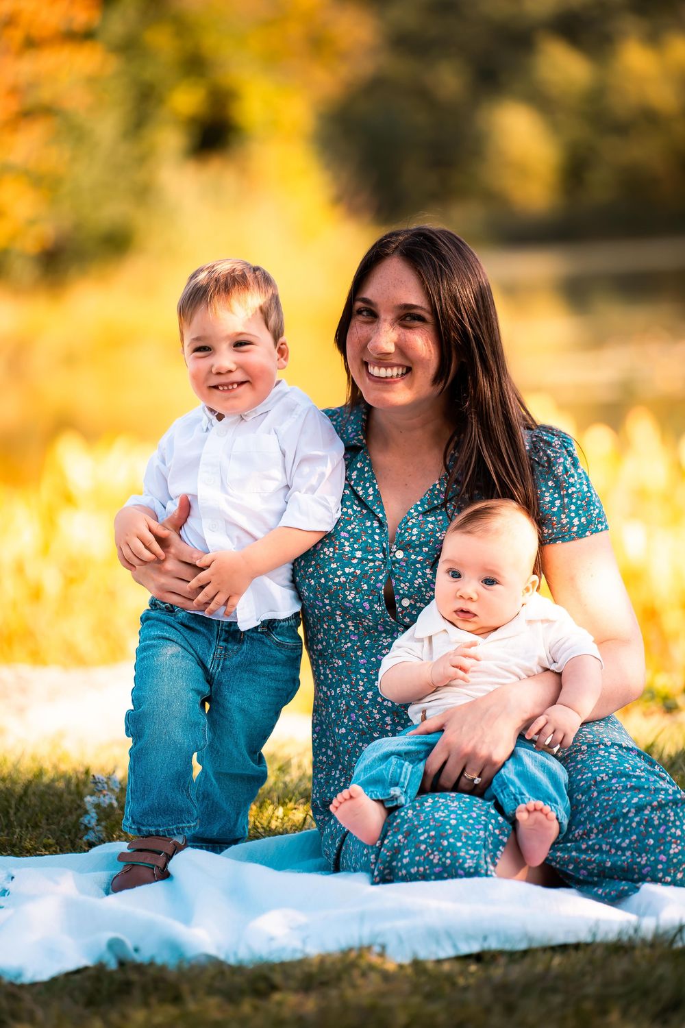Family sits together on white blanket during golden hour autumn photoshoot in field.