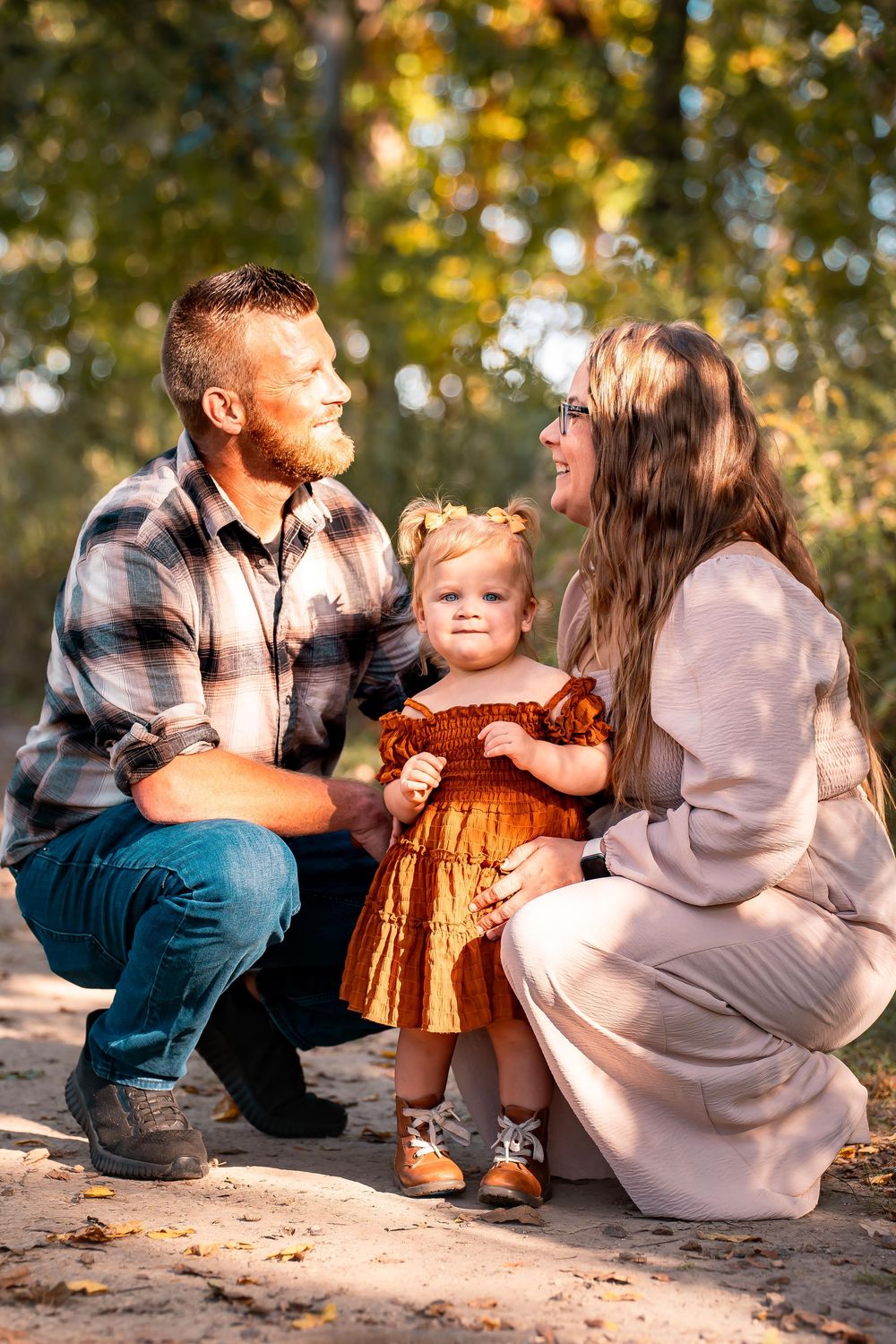 Family sitting together on ground during autumn photoshoot with warm lighting.