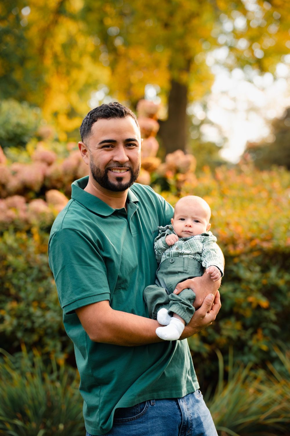 Outdoor portrait session in autumn garden with green-shirted adult holding baby.