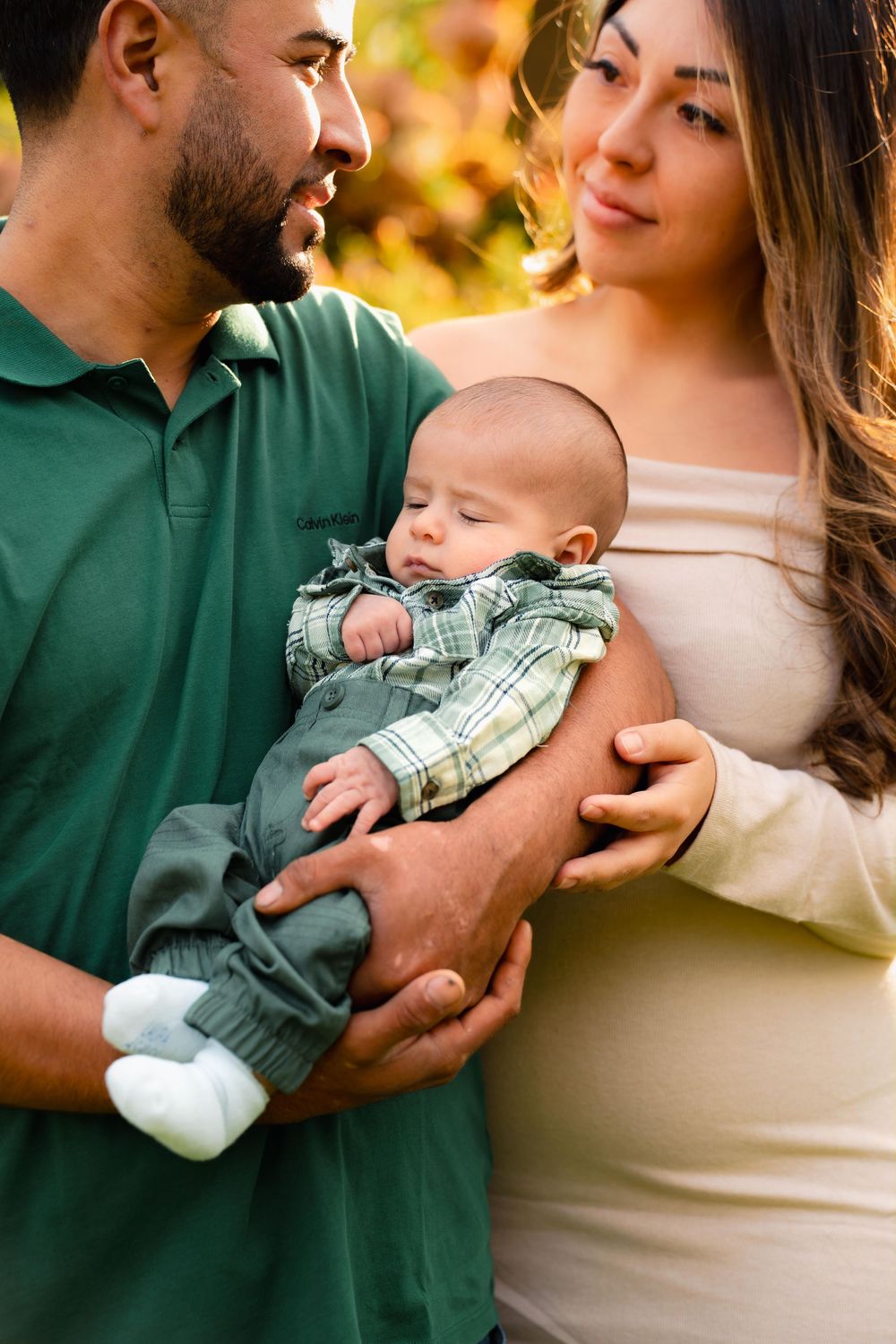 Intimate family moment captured with baby in green outfit during sunset photoshoot.