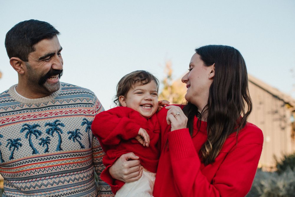 A family wearing holiday sweaters shares a joyful moment together outdoors during sunset.