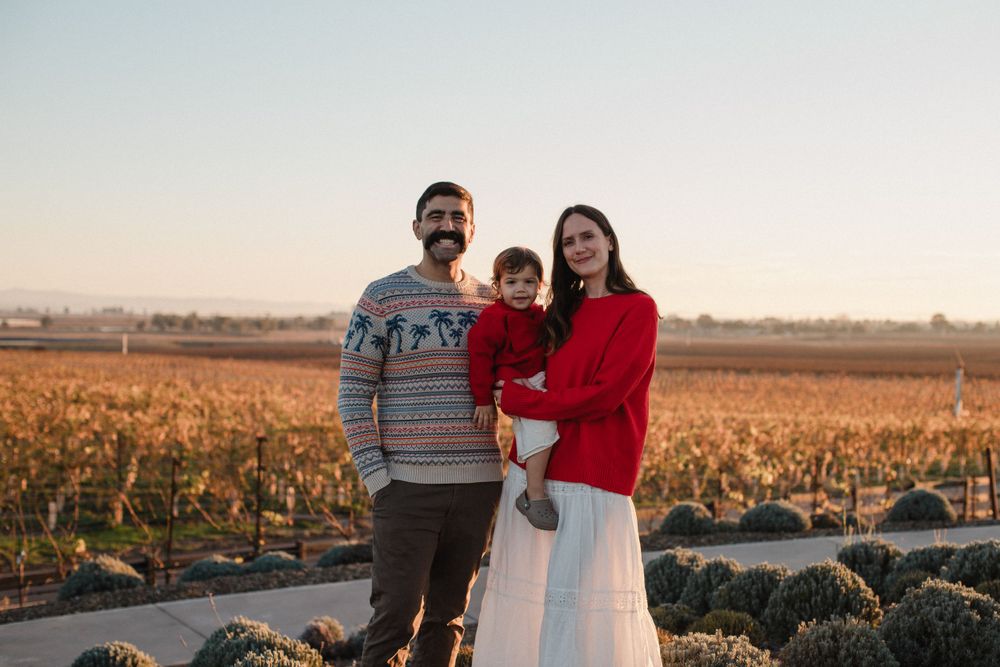 A smiling family poses in front of rows of golden grapevines during sunset.