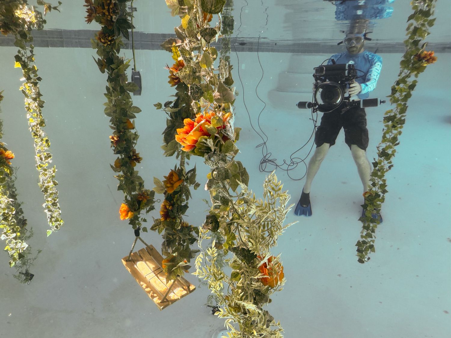 Scuba diver and underwater photographer exploring underwater columns decorated with glowing lights and orange flowers in clear blue water.