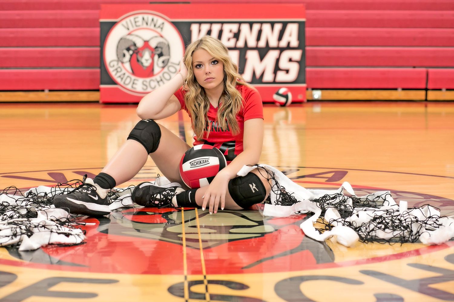 Athletic photo shoot on gymnasium floor with sports equipment and red backdrop.