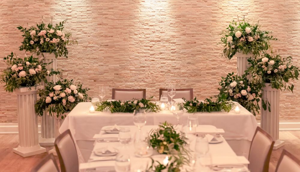 Elegant wedding reception table setup with white linens, columns and blush floral arrangements against a peachy textured wall.