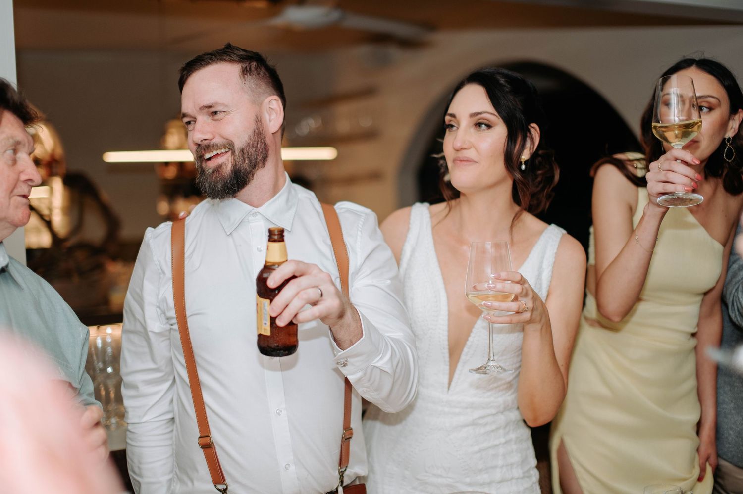 Wedding celebration with guests enjoying drinks and laughter at an indoor reception.