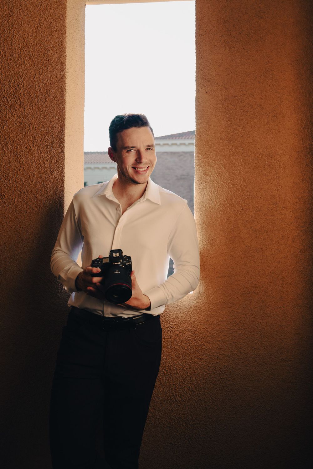 Professional photographer holding camera while standing in doorway with warm lighting.