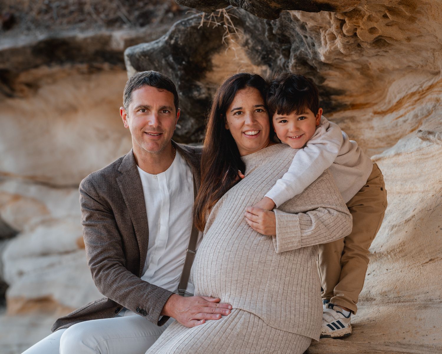 A young boy hugs his dad while his mom holds his hand during a family photoshoot at Balmoral Beach in Mosman