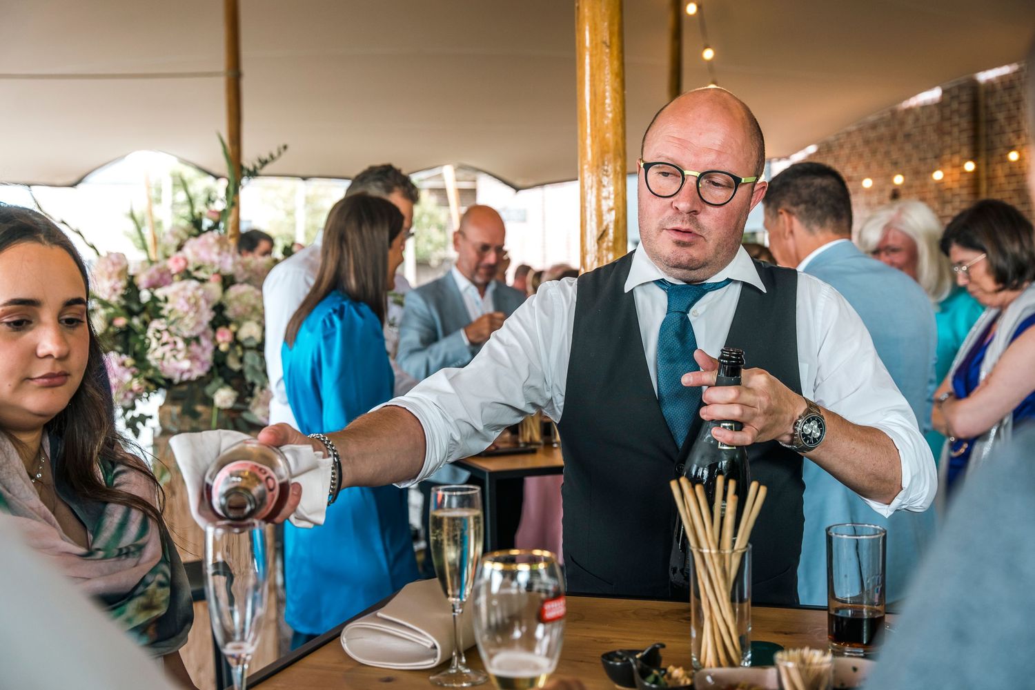Reception bartender serving drinks to wedding guests at indoor venue.