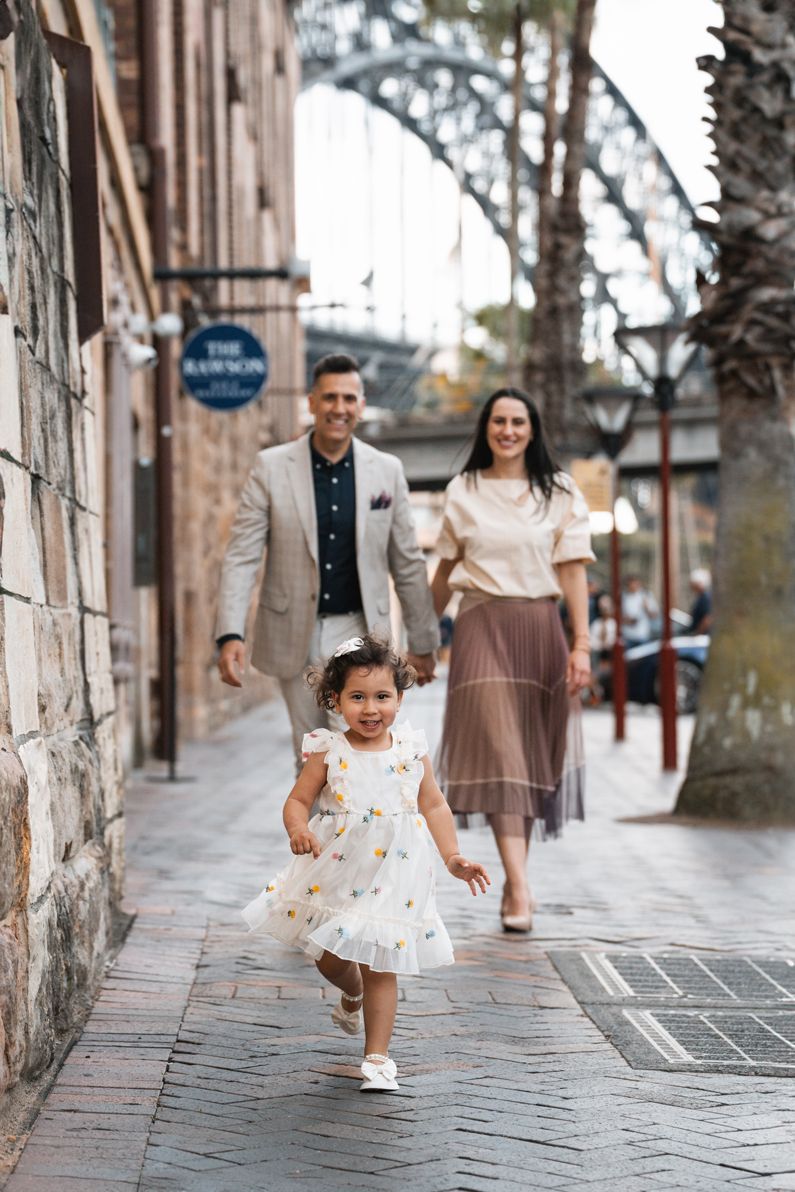 happy-girl-running-towards-the-camera-during-family-photoshoot-in-the-streets-of-sydney-with-the-harbour-bridge