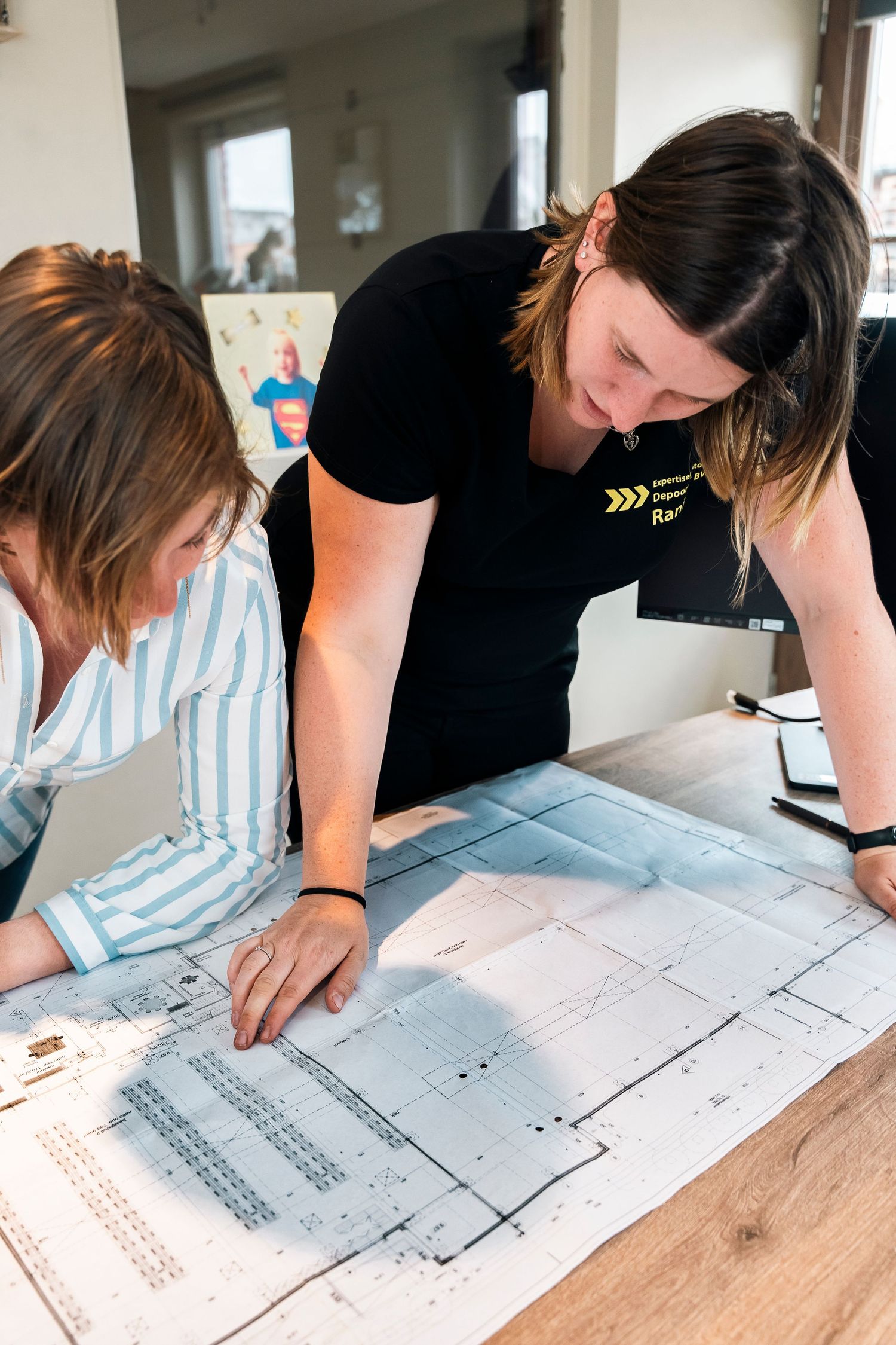 Two people reviewing technical documents and blueprints on wooden table.