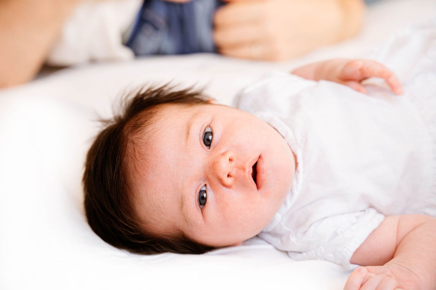 Baby in white clothing lying on soft white bedding.