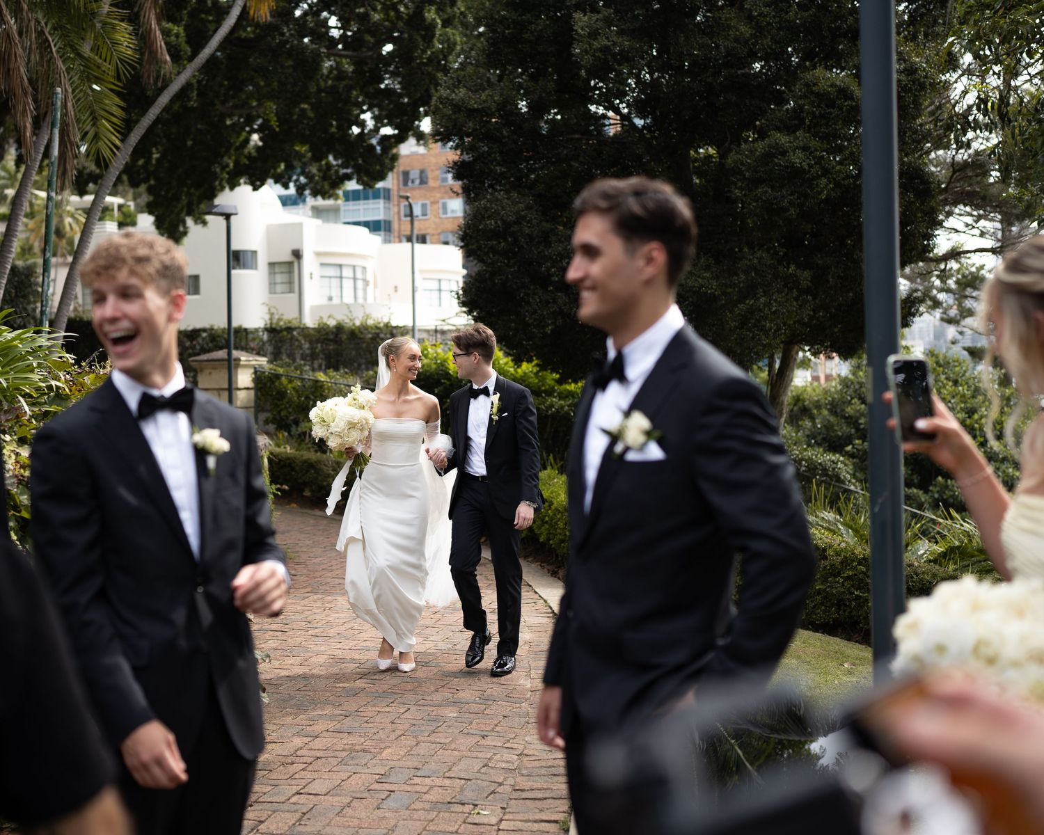 Wedding party walking along garden path with festive celebration.