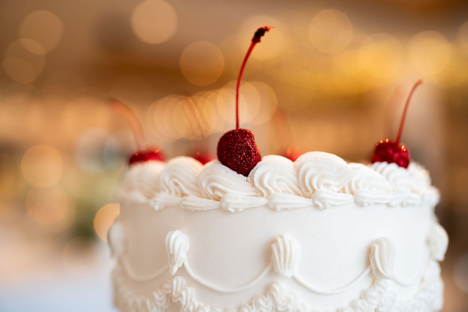 Elegant white wedding cake decorated with whipped cream and fresh red cherries on top.