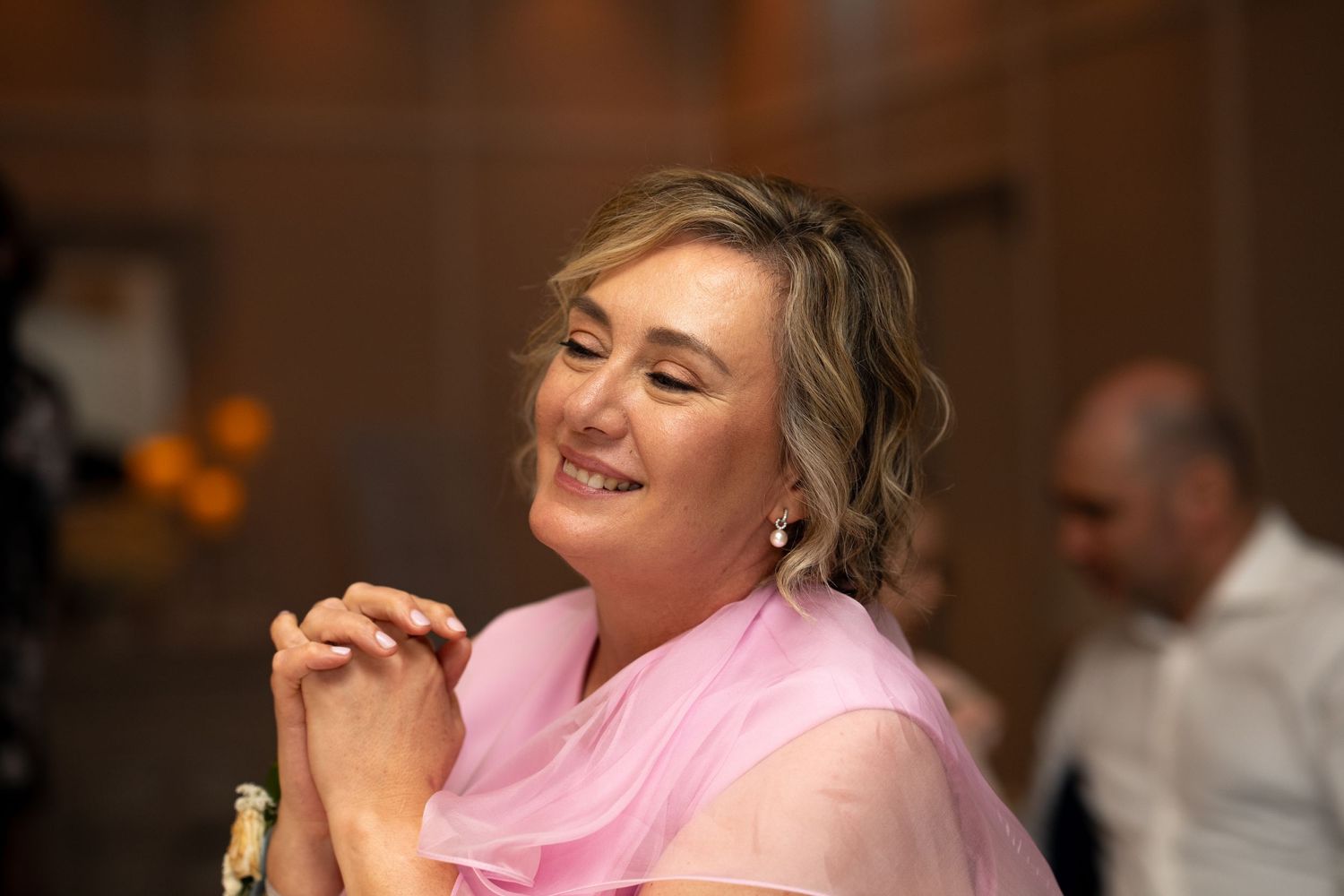 A guest at a wedding reception wearing a pink shawl smiles while seated at a table.
