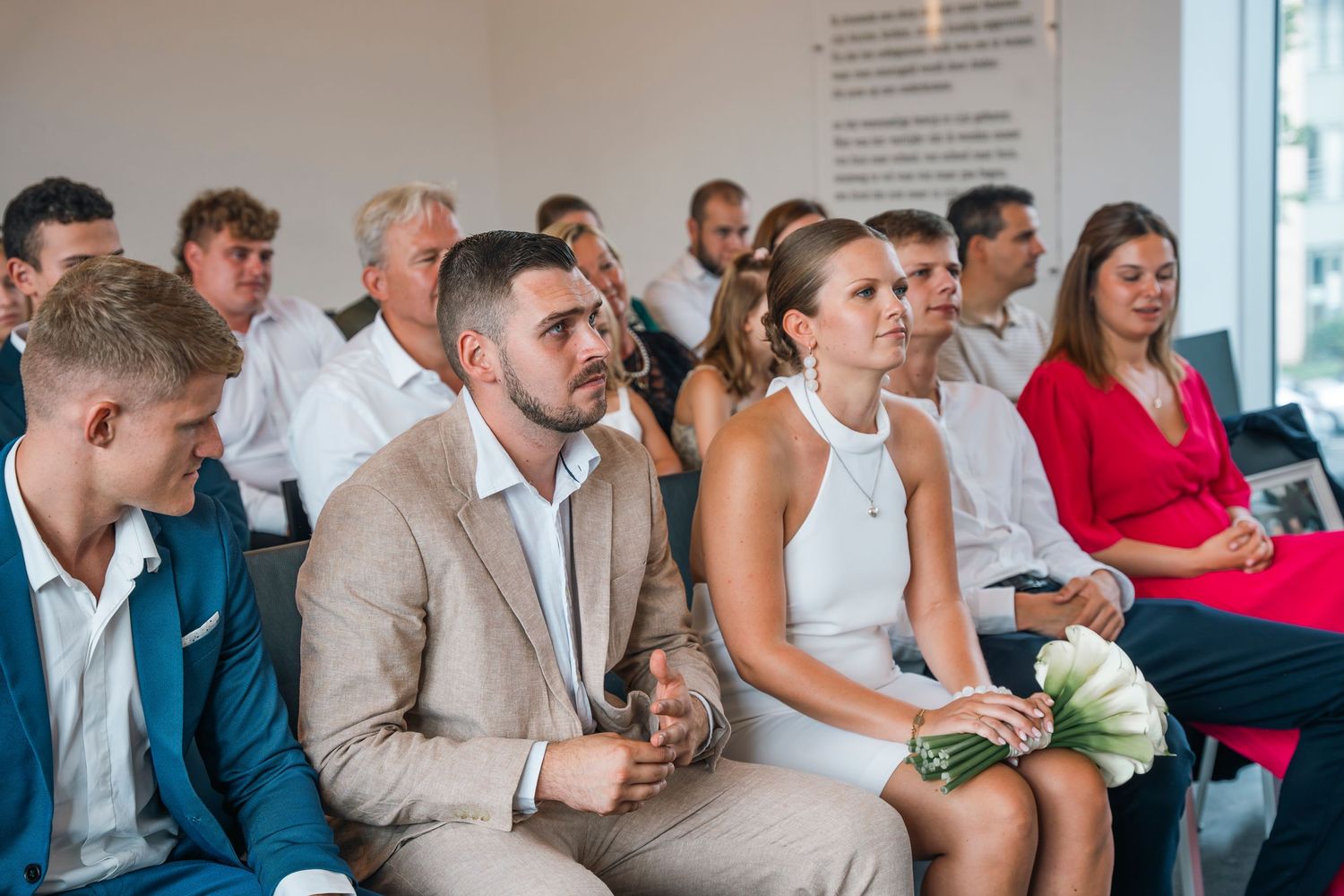 Wedding guests seated in casual attire watch ceremony proceedings indoors.
