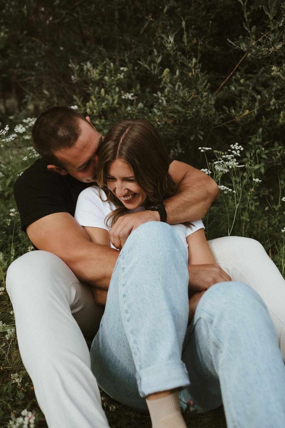 Candid moment of playful embrace on grassy ground with wildflowers.