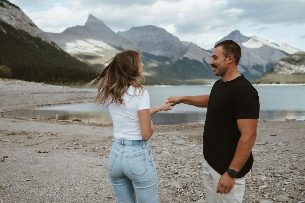Couple holding hands while walking along rocky mountain lakeshore.