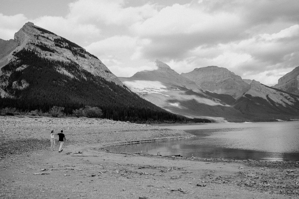 Black and white landscape of mountain lake with distant figure on shoreline.