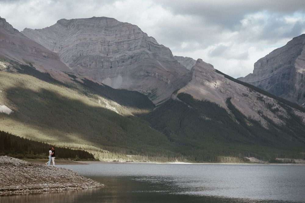 Dramatic mountain vista with lone figure walking along misty lakeshore.