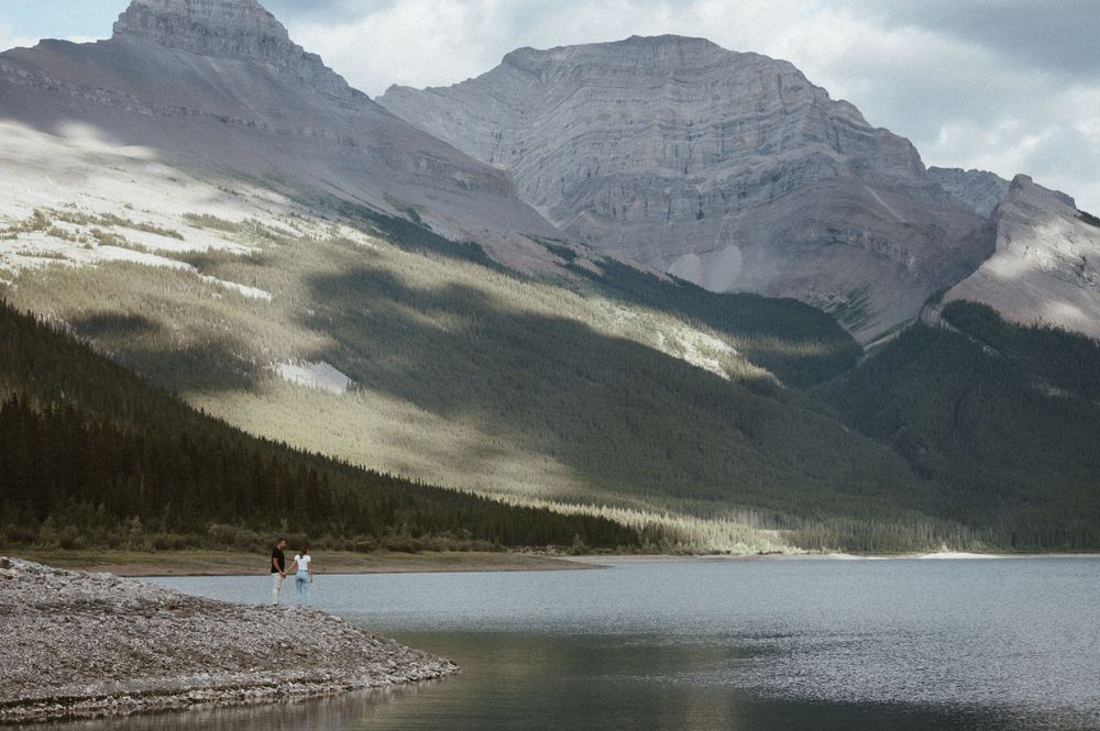 Scenic mountain lake surrounded by towering peaks with figure on rocky shore.
