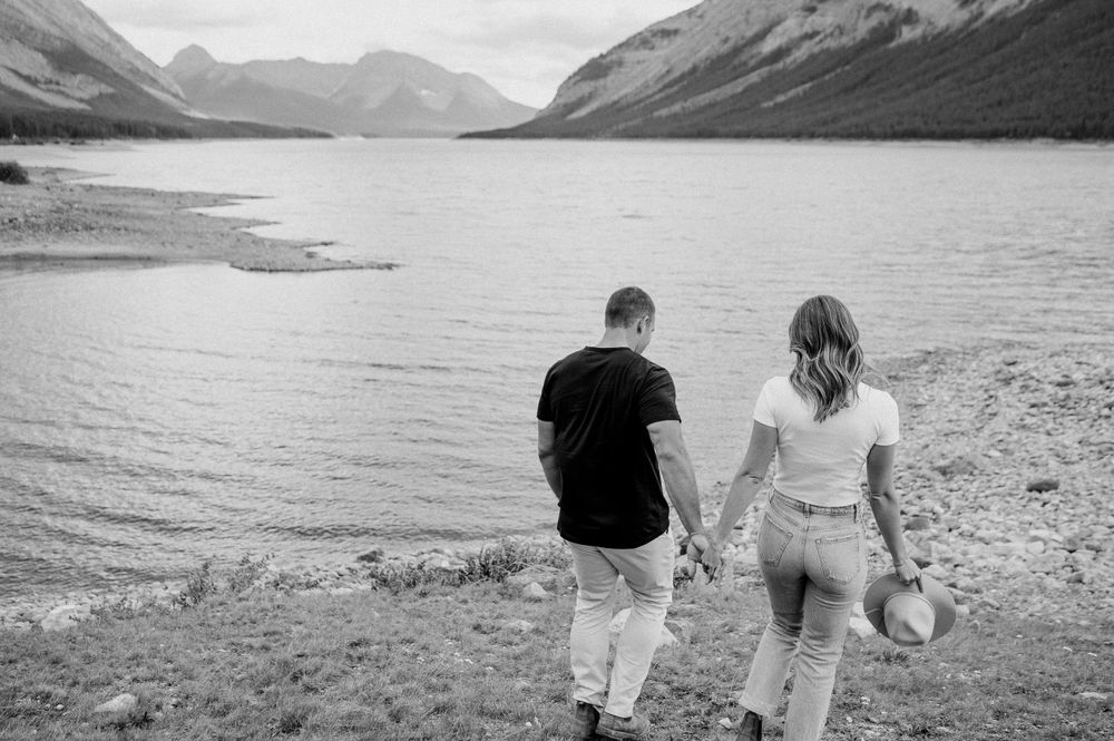Black and white photo of a couple walking together along a mountain lake shoreline.
