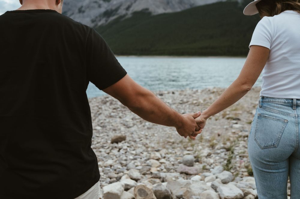 Close-up of clasped hands as couple walks on rocky mountain shoreline.