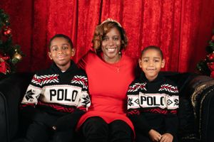 Three people wearing matching Polo sweaters pose together on a couch against a red backdrop with Christmas decor.