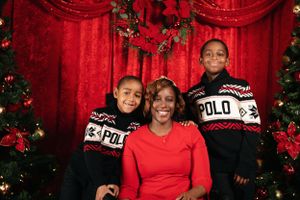 Three people in matching Polo sweaters pose for a holiday photo with Christmas decorations.