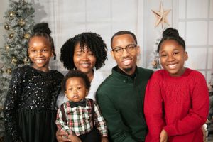 Holiday family portrait in front of Christmas tree with sparkly black dress, plaid outfit, green sweater and red sweater.