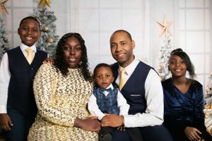 Formal family portrait with gold and navy outfits in front of Christmas decorations.