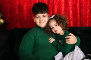 Two people in matching green sweaters share warm holiday moment against red backdrop.