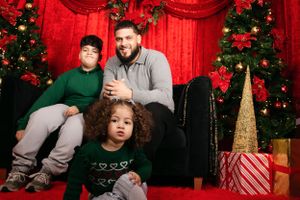 Family relaxing on black couch with Christmas decorations and presents in background.