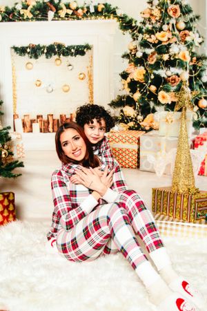 A pair in matching plaid pajamas share a holiday moment in front of a decorated Christmas tree and presents.