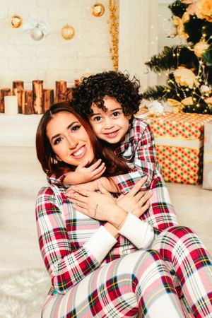 Two people in matching plaid pajamas share a warm embrace during a holiday photoshoot.