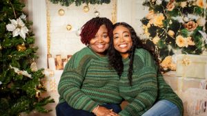 Two people wearing matching green sweaters share a joyful moment by a Christmas tree.