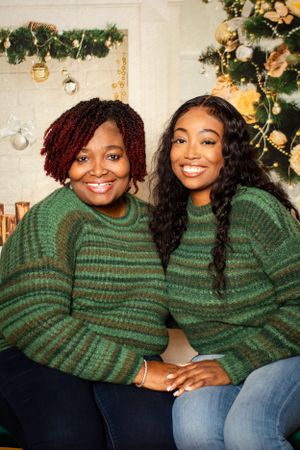 Two people in matching green striped sweaters smile together near holiday decorations.