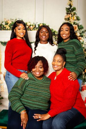 Group wearing festive red and green sweaters pose together by Christmas decorations.