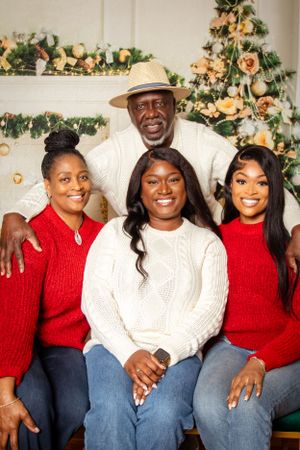 Family members in coordinated red and white sweaters sit together by holiday decorations.