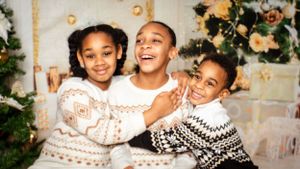 Three children in festive winter sweaters share a joyful holiday moment together.