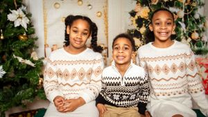 Three children in Nordic pattern sweaters pose together for a holiday portrait.