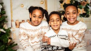 Three children wearing matching winter sweaters smile for a Christmas photo.